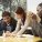 A photograph showing a woman helping two men with English language lessons.